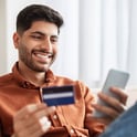 Hombre pagando el total de su tarjeta de crédito usando su teléfono celular.