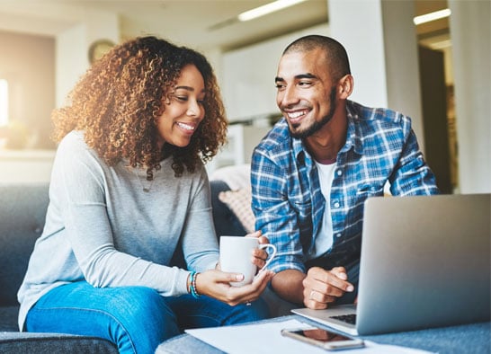 Couple-discussing-the-benefits-of-solar-energy-on-couch-with-laptop-and-coffee