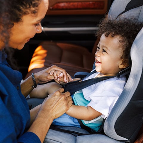 Mom-used-a-fast-cash-loan-to-fix-her-car-and-is-now-safely-buckling-her-son-in-the-carseat-as-he-smiles-back-at-her.