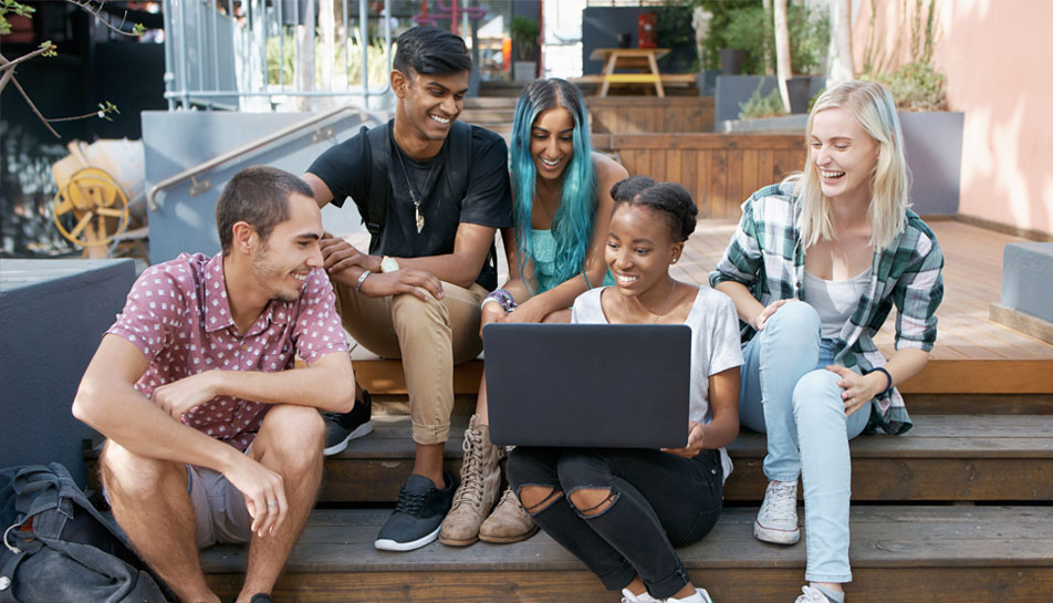 Group-of-diverse-teens-on-a-laptop-deciding-if-a-credit-union-or-bank-is-best-for-them-while-sitting-on-stairs-outside.