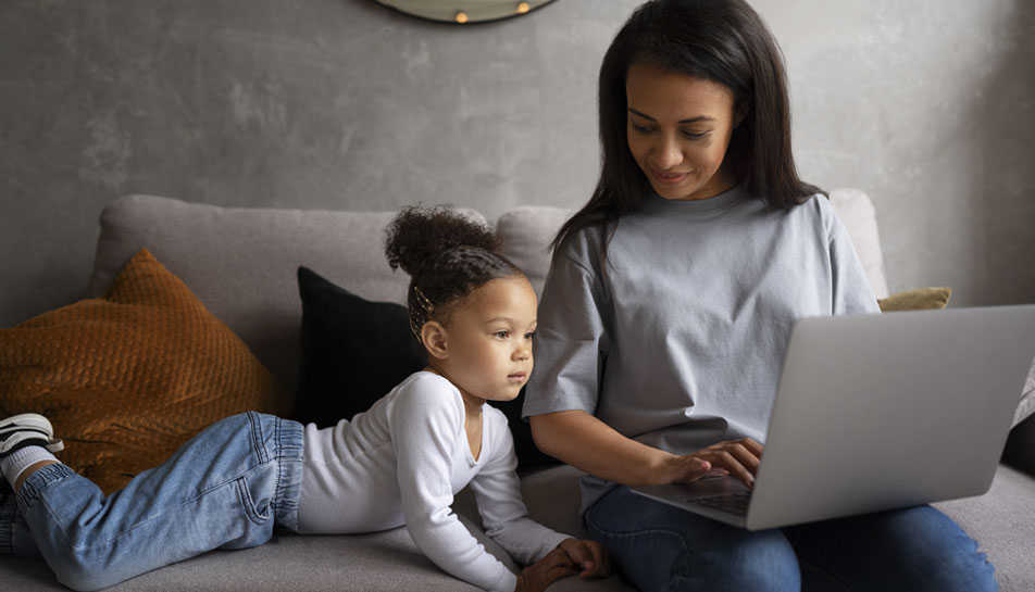 Mom-researching-to-best-way-to-save-money-for-your-kids-on-her-laptop-while-sitting-on-the-couch-with-her-daughter.